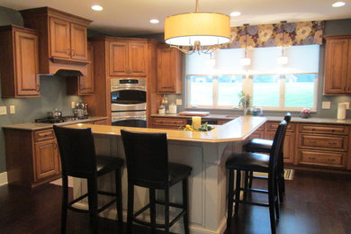 Example of a mid-sized classic u-shaped dark wood floor eat-in kitchen design in Cincinnati with an undermount sink, raised-panel cabinets, medium tone wood cabinets, quartz countertops, stainless steel appliances and an island
