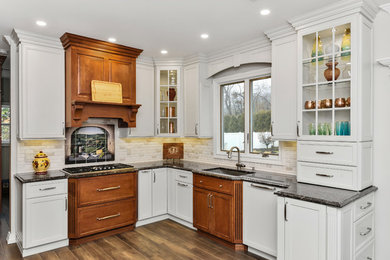 Mid-sized transitional l-shaped porcelain tile and brown floor eat-in kitchen photo in New York with an undermount sink, recessed-panel cabinets, white cabinets, granite countertops, white backsplash, porcelain backsplash, stainless steel appliances, a peninsula and brown countertops