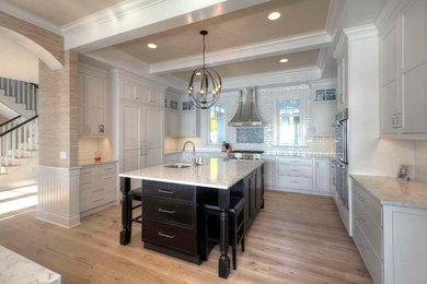 Foto de cocina clásica renovada con fregadero sobremueble, puertas de armario blancas, salpicadero blanco, electrodomésticos de acero inoxidable, suelo de madera clara y una isla