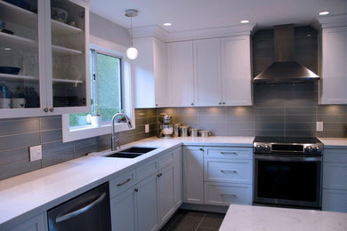 Enclosed kitchen - transitional l-shaped porcelain tile enclosed kitchen idea in Vancouver with an undermount sink, shaker cabinets, white cabinets, quartz countertops, gray backsplash, glass tile backsplash and stainless steel appliances