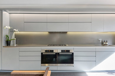 Photo of a medium sized contemporary single-wall open plan kitchen in London with a built-in sink, flat-panel cabinets, grey cabinets, composite countertops, grey splashback, glass sheet splashback, stainless steel appliances, ceramic flooring, no island, grey floors and grey worktops.