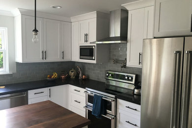 Example of a mid-sized 1960s l-shaped light wood floor eat-in kitchen design in Seattle with a farmhouse sink, shaker cabinets, white cabinets, soapstone countertops, green backsplash, ceramic backsplash, stainless steel appliances, an island and gray countertops