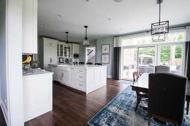 Inspiration for a large timeless l-shaped medium tone wood floor eat-in kitchen remodel in Indianapolis with a farmhouse sink, shaker cabinets, white cabinets, granite countertops, white backsplash, ceramic backsplash, paneled appliances, an island and white countertops