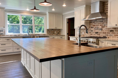 Classic l-shaped kitchen in Austin with a belfast sink, shaker cabinets, white cabinets, wood worktops, brick splashback, stainless steel appliances, medium hardwood flooring, an island and a timber clad ceiling.