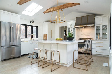 Photo of a large traditional l-shaped kitchen in Chicago with a submerged sink, shaker cabinets, white cabinets, engineered stone countertops, grey splashback, marble splashback, stainless steel appliances, light hardwood flooring, an island and brown floors.