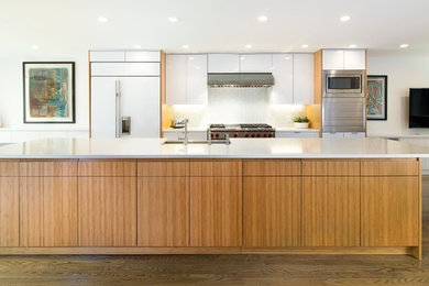 Photo of a large contemporary galley open plan kitchen in New York with a submerged sink, flat-panel cabinets, white cabinets, granite worktops, white splashback, glass tiled splashback, stainless steel appliances, dark hardwood flooring and an island.