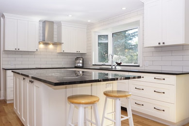 Eat-in kitchen - mid-sized transitional l-shaped light wood floor eat-in kitchen idea in Calgary with an undermount sink, shaker cabinets, white cabinets, granite countertops, white backsplash, an island and black countertops