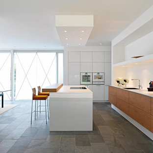 Cette photo montre une cuisine américaine parallèle moderne avec un placard à porte plane, des portes de placard en bois brun, un électroménager blanc et un sol en ardoise.