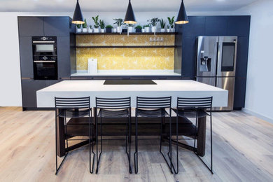 Inspiration for a medium sized contemporary galley kitchen/diner in London with a submerged sink, flat-panel cabinets, blue cabinets, quartz worktops, yellow splashback, ceramic splashback, stainless steel appliances, light hardwood flooring, an island, beige floors and white worktops.
