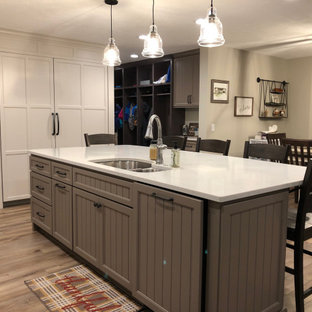 Expansive transitional u-shaped open plan kitchen in Grand Rapids with an undermount sink, recessed-panel cabinets, white cabinets, quartz benchtops, multi-coloured splashback, ceramic splashback, stainless steel appliances, vinyl floors, with island, brown floor and white benchtop.