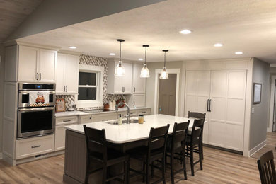 Large transitional u-shaped vinyl floor and brown floor open concept kitchen photo in Grand Rapids with an undermount sink, recessed-panel cabinets, white cabinets, quartz countertops, multicolored backsplash, ceramic backsplash, stainless steel appliances, an island and white countertops