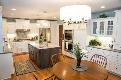 Farmhouse u-shaped medium tone wood floor and brown floor eat-in kitchen photo in Chicago with white cabinets, white backsplash, stainless steel appliances, an island, gray countertops, a drop-in sink, shaker cabinets and ceramic backsplash
