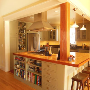 Mid-sized contemporary u-shaped eat-in kitchen in Burlington with a farmhouse sink, shaker cabinets, green cabinets, stainless steel appliances, light hardwood floors, with island and wood benchtops.