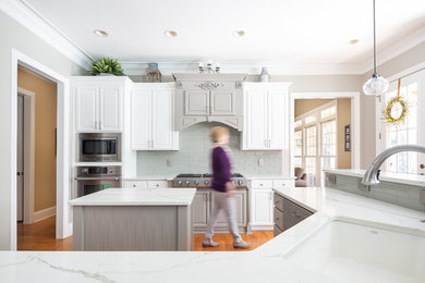 Mid-sized transitional light wood floor kitchen photo in Dallas with an undermount sink, raised-panel cabinets, white cabinets, quartz countertops, gray backsplash, glass tile backsplash, stainless steel appliances and two islands
