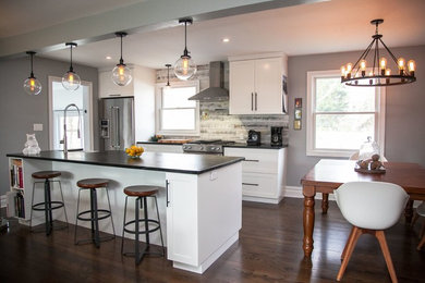 Example of a mid-sized minimalist galley dark wood floor and brown floor eat-in kitchen design in New York with a farmhouse sink, shaker cabinets, white cabinets, quartz countertops, gray backsplash, wood backsplash, stainless steel appliances and an island