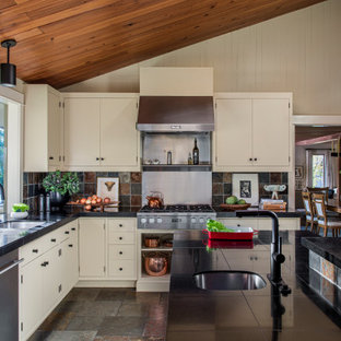 Large midcentury l-shaped kitchen in Portland with a double-bowl sink, flat-panel cabinets, beige cabinets, granite benchtops, multi-coloured splashback, slate splashback, stainless steel appliances, slate floors, with island, brown floor, black benchtop and wood.