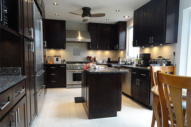 Example of a mid-sized classic u-shaped porcelain tile eat-in kitchen design in Milwaukee with a farmhouse sink, shaker cabinets, black cabinets, granite countertops, white backsplash, ceramic backsplash, stainless steel appliances and an island