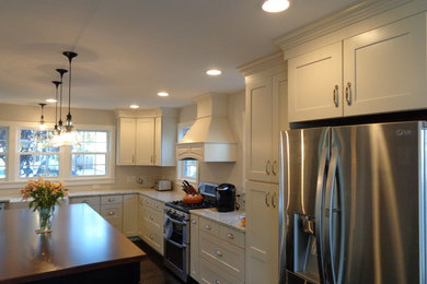 Classic l-shaped kitchen/diner in New York with a belfast sink, recessed-panel cabinets, white cabinets, wood worktops and stainless steel appliances.