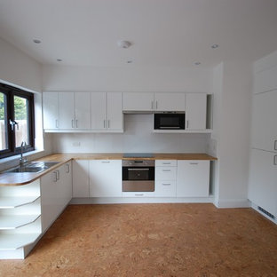 Imagen de cocina comedor en L, contemporánea, de tamaño medio, con fregadero encastrado, armarios con paneles lisos, puertas de armario blancas, encimera de madera, salpicadero blanco, salpicadero de vidrio templado, electrodomésticos de acero inoxidable y suelo de corcho
