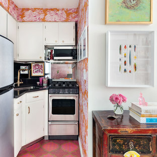 This is an example of a small eclectic open plan kitchen in New York with an undermount sink, flat-panel cabinets, white cabinets, black splashback, stainless steel appliances, no island, pink floor and black benchtop.