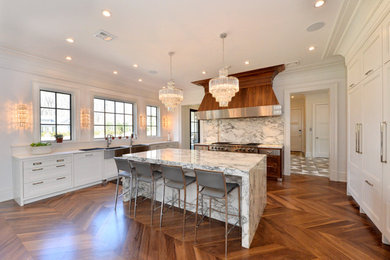 Eat-in kitchen - large transitional u-shaped medium tone wood floor and brown floor eat-in kitchen idea in New York with a farmhouse sink, shaker cabinets, white cabinets, marble countertops, white backsplash, stone slab backsplash, paneled appliances and an island