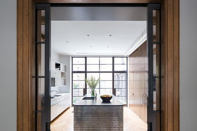 Example of a large eclectic u-shaped light wood floor and brown floor enclosed kitchen design in New York with an undermount sink, flat-panel cabinets, white cabinets, solid surface countertops, paneled appliances and an island