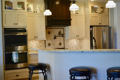 Inredning av ett klassiskt mellanstort kök, med en undermonterad diskho, skåp i shakerstil, vita skåp, granitbänkskiva, beige stänkskydd, stänkskydd i mosaik, rostfria vitvaror, mellanmörkt trägolv, en halv köksö och brunt golv