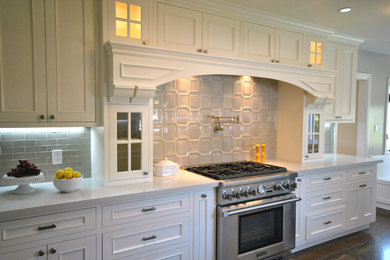 Klassisk inredning av ett kök, med en undermonterad diskho, luckor med profilerade fronter, vita skåp, bänkskiva i kvarts, beige stänkskydd, stänkskydd i keramik, rostfria vitvaror och mörkt trägolv