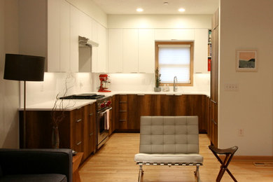 Example of a mid-sized minimalist u-shaped light wood floor open concept kitchen design in Minneapolis with flat-panel cabinets, white cabinets, white backsplash, stainless steel appliances, no island and white countertops