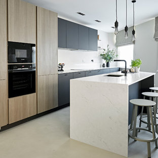 Photo of a small contemporary kitchen in London with a submerged sink, flat-panel cabinets, marble worktops, black appliances, an island, grey floors, white worktops, black cabinets and concrete flooring.