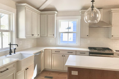 Kitchen - mid-sized l-shaped light wood floor kitchen idea in Cleveland with a farmhouse sink, recessed-panel cabinets, quartz countertops, white backsplash, subway tile backsplash, stainless steel appliances, an island and white countertops