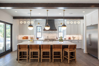 Inspiration for a large country l-shaped medium tone wood floor and brown floor open concept kitchen remodel in San Francisco with a farmhouse sink, shaker cabinets, white cabinets, quartz countertops, gray backsplash, marble backsplash, stainless steel appliances, an island and white countertops