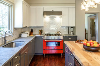 Example of a large farmhouse l-shaped dark wood floor enclosed kitchen design in New York with an undermount sink, gray cabinets, solid surface countertops, white backsplash, subway tile backsplash, colored appliances, an island and shaker cabinets