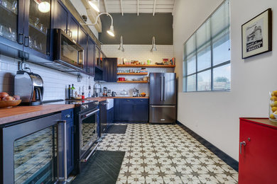 Enclosed kitchen - mid-sized transitional l-shaped ceramic tile and multicolored floor enclosed kitchen idea in San Francisco with a farmhouse sink, shaker cabinets, blue cabinets, wood countertops, white backsplash, subway tile backsplash, stainless steel appliances, no island and brown countertops