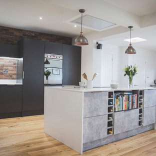 Design ideas for a contemporary l-shaped kitchen/diner in Devon with flat-panel cabinets, grey cabinets, an island, red splashback, stainless steel appliances, medium hardwood flooring and brown floors.