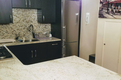 Example of a mid-sized minimalist u-shaped porcelain tile and beige floor enclosed kitchen design in New York with a single-bowl sink, flat-panel cabinets, brown cabinets, granite countertops, metallic backsplash, glass tile backsplash, stainless steel appliances, a peninsula and white countertops