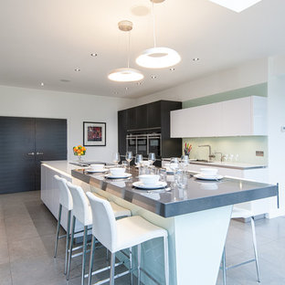 Inspiration for a large contemporary single-wall eat-in kitchen in London with flat-panel cabinets, grey cabinets, stainless steel appliances, with island, an undermount sink, white splashback, glass sheet splashback and porcelain floors.