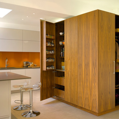 Example of a large trendy kitchen design in London with an island, flat-panel cabinets, medium tone wood cabinets, solid surface countertops, orange backsplash, glass sheet backsplash and an undermount sink