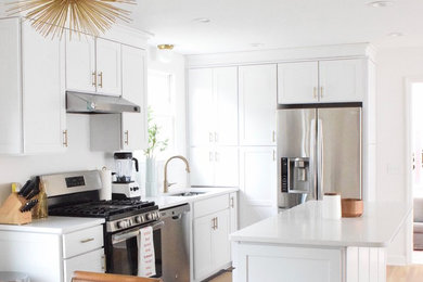 Bild på ett mellanstort funkis kök och matrum, med vita skåp, marmorbänkskiva, vitt stänkskydd, stänkskydd i tunnelbanekakel, rostfria vitvaror, ljust trägolv, en köksö och brunt golv