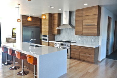 Foto på ett mellanstort funkis kök och matrum, med en undermonterad diskho, skåp i mellenmörkt trä, bänkskiva i kvarts, rostfria vitvaror, ljust trägolv och en köksö