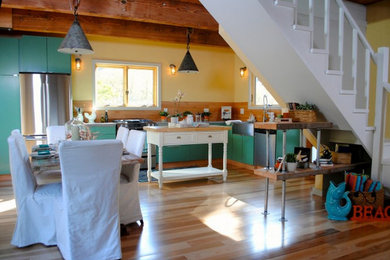 Example of a mid-sized beach style l-shaped light wood floor eat-in kitchen design in San Francisco with a farmhouse sink, flat-panel cabinets, quartz countertops, stainless steel appliances and an island