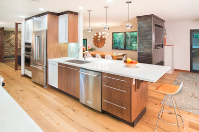 Mid-sized trendy galley light wood floor enclosed kitchen photo in San Francisco with an undermount sink, flat-panel cabinets, medium tone wood cabinets, glass countertops, green backsplash, glass tile backsplash, stainless steel appliances and a peninsula