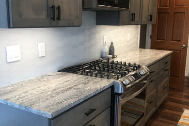 Example of a mid-sized trendy galley vinyl floor and brown floor eat-in kitchen design in Minneapolis with a farmhouse sink, shaker cabinets, gray cabinets, quartzite countertops, white backsplash, glass tile backsplash, stainless steel appliances and gray countertops