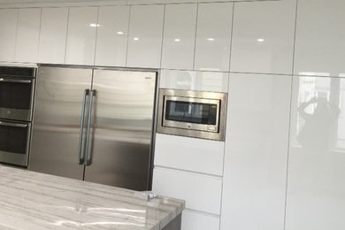 Example of a large minimalist enclosed kitchen design in New York with an undermount sink, flat-panel cabinets, white cabinets, stainless steel appliances, an island and quartzite countertops