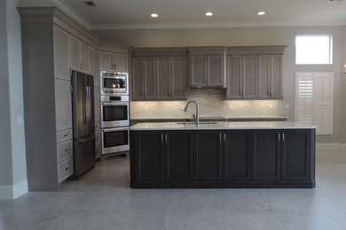 Modern inredning av ett stort kök, med en undermonterad diskho, luckor med infälld panel, grå skåp, bänkskiva i kvartsit, grått stänkskydd, stänkskydd i stickkakel, rostfria vitvaror, klinkergolv i keramik, en köksö och grått golv