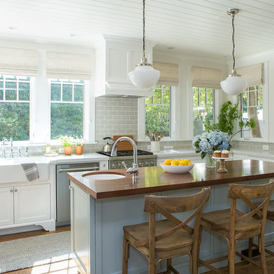 Eat-in kitchen - mid-sized coastal u-shaped medium tone wood floor and brown floor eat-in kitchen idea in Santa Barbara with a farmhouse sink, shaker cabinets, white cabinets, wood countertops, gray backsplash, subway tile backsplash, stainless steel appliances and an island