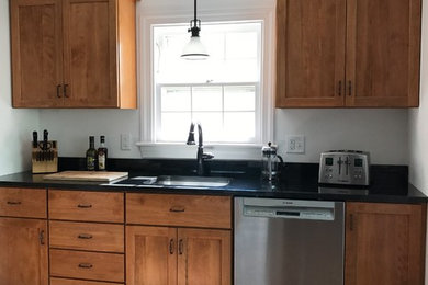 This is an example of a medium sized country single-wall enclosed kitchen in Burlington with a submerged sink, shaker cabinets, medium wood cabinets, engineered stone countertops, stainless steel appliances, terracotta flooring, no island, orange floors and black worktops.