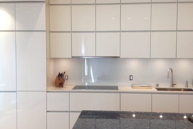 Foto på ett mellanstort funkis blå linjärt kök och matrum, med en undermonterad diskho, släta luckor, vita skåp, granitbänkskiva, vitt stänkskydd, glaspanel som stänkskydd, rostfria vitvaror, ljust trägolv, en köksö och brunt golv