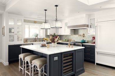 Klassisk inredning av ett vit vitt l-kök, med en rustik diskho, luckor med infälld panel, blå skåp, grått stänkskydd, integrerade vitvaror, ljust trägolv, en köksö och beiget golv