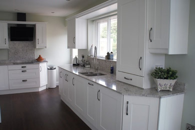 Diseño de cocina contemporánea de tamaño medio con fregadero bajoencimera, armarios estilo shaker, puertas de armario blancas, encimera de granito, salpicadero verde, electrodomésticos negros y encimeras grises